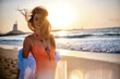 Cheerful woman with hair tousled by the wind on the beach at sunset, with sun flares