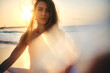 A woman poses with the sun setting at her back, creating a beautiful lens flare and silhouette effect on the beach