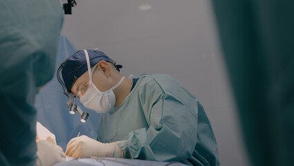 Surgeon man practitioner with team assistants perform surgical operation doctor sewing up wound sutures skin with medical tools clips thread in hospital operating room patient health treatment surgery