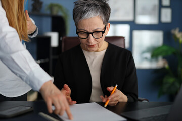 In the office, cooperation is evident as businesswoman leads a team meeting, discussing documents and plans.