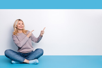 Sticker - Full body photo of senior lady sit floor crossed legs point empty space dressed stylish gray garment isolated on blue color background