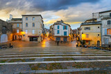 Fototapeta Uliczki - Illuminated shops and cafes after an evening rain seen from the steps of the ancient arena in the historic medieval old town of Arles, France, in the Provence region.