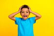 Photo of speechless crazy kid with curly hair dressed blue t-shirt keep hands on head staring isolated on vibrant yellow background