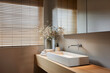 A modern bathroom with wooden blinds and a white sink, featuring an elegant display of flowers on the counter. The scene is captured in a closeup shot, showcasing details like a sleek faucet.