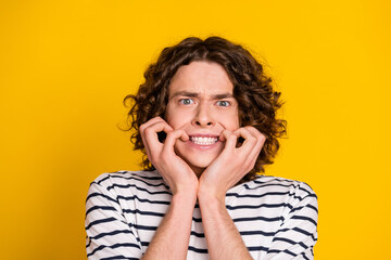 Poster - Portrait of young wavy hair guy wearing striped t shirt grinning nails nervous before exam in college isolated on yellow color background