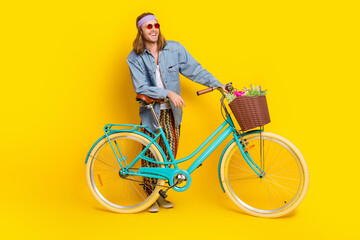 Sticker - Full body portrait of cool young man bicycle look empty space wear denim shirt isolated on yellow color background