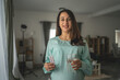 © Miljan Živković - Adult pregnant women stand and hold medicament glass of water at home