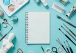 A blank white spiral notebook is centered on the page, surrounded by various art supplies such as paintbrushes and paper dolls.