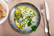 There is portion of breakfast on table - omelet with spinach, decorated with sprig of parsley, slices of bran bread
