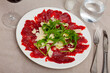 Delicious beef carpaccio with grated hard cheese and aromatic arugula served on plate. Meat appetizer..