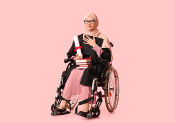 Wall Mural - Beautiful female Muslim graduate student in wheelchair with diploma, graduation cap and books on pink background