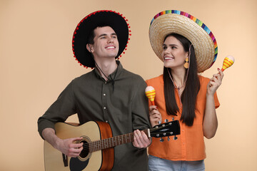 Lovely couple woman in Mexican sombrero hats with maracas and guitar on beige background