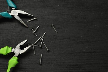 Canvas Print - Pliers and nails on black wooden table, flat lay. Space for text