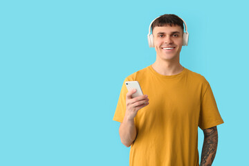 Poster - Handsome young happy man in headphones with mobile phone listening audiobook on blue background