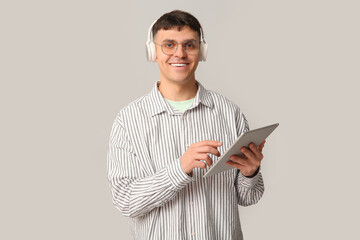 Poster - Handsome young happy man in headphones with tablet listening audiobook on grey background