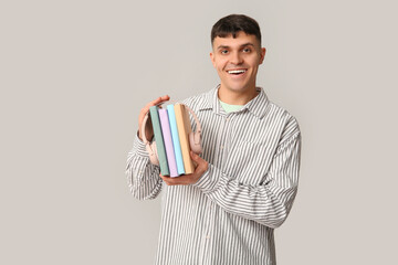 Poster - Handsome young happy man with headphones and books stack on grey background. Concept of audiobook