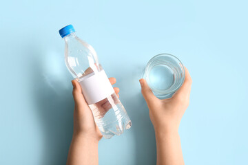 Wall Mural - Female hands with plastic bottle of clean water and glass on blue background