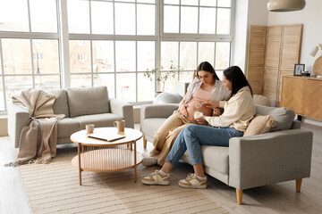 Canvas Print - Young pregnant woman with wife applying cream on her belly at home