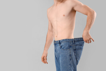 Sticker - Handsome young sporty man in loose jeans on grey background, closeup. Weight loss concept