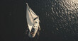 Top down of yacht under white sail at dark open sea aerial. Ocean bay black water and lonely sailboat. Summer cruise on boat. Luxury yachting scenery at serene seascape in dramatic drone shot