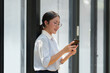 Happy Asian businesswoman in glasses standing smiling looking at data Talk on the phone using your smartphone for communication. Check through the application Go online while in the modern office.