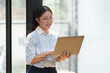 © crizzystudio - A beautiful businesswoman wearing glasses stands happily smiling and expressing joy while doing business online finance Approval of investment and notebook computers in the office.