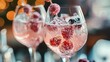 Close up of two nicely decorated cocktail glasses filled with a pink gin tonic beverage with frozen berries