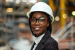 A woman, wearing a hard hat and safety glasses, is at a construction site, supervising or working on a project. She appears focused and professional, ensuring safety and compliance