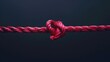 A red rope with two knotted ends on a dark background, symbolizing strength and unity .