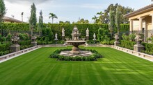 An Elegant Backyard With A Manicured Lawn And A Classic Fountain In The Center. Ornate Garden Statues Are Strategically Placed, And There Are Neatly Trimmed Hedges Along The Fence. 