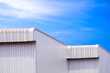 Two modern metal industrial warehouse buildings with aluminium roof eaves against blue sky background, perspective side view with copy space 
