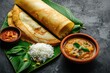 South Indian Traditional Dishes arranged on banana leaf, including rice, several kinds of curry and dosa or flatbread roll. Ready to be enjoyed on dining table.