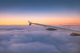 Fototapeta Natura - Airplane flying over color sky clouds during scenic sunset or sunrise cloudscape, view from plane window of wing turbines and horizon