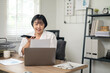 © Wasana - Cheerful businesswoman in white shirt using smartphone with laptop and documents on her office desk.