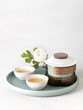 Asian tea modern ceremony set with crystal pot and ceramic bowl cup with green tea on a try with white flowers