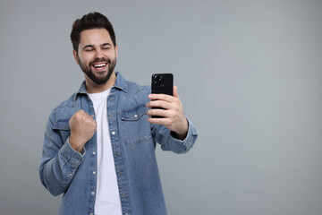 Sticker - Happy young man using smartphone on grey background, space for text