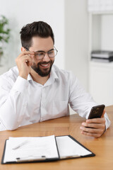 Wall Mural - Handsome young man using smartphone at wooden table in office