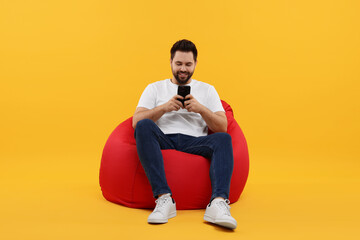 Canvas Print - Happy young man using smartphone on bean bag chair against yellow background