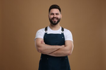 Canvas Print - Smiling man in kitchen apron with crossed arms on brown background. Mockup for design