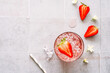 Ein Sommer Getränk mit Eiswürfel und Erdbeeren in einem Trinkglas auf einem grauen Kachel Tisch. Draufsicht.