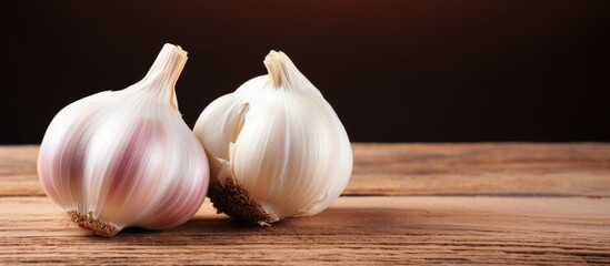 Fototapete - Two garlic bulbs on wooden table with dark backdrop