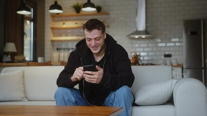 Smiling man sitting on couch using smartphone check message read notice receive good news on e-mail celebrate great opportunity feels happy 
