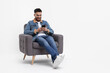 © New Africa - Happy man using smartphone in armchair on white background, space for text