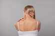 © New Africa - Woman suffering from pain in her neck on grey background, back view