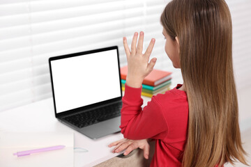 Wall Mural - E-learning. Girl raising her hand to answer during online lesson at table indoors