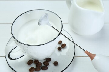 Sticker - Mini mixer (milk frother), whipped milk and coffee beans on white wooden table, closeup