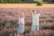Friends raised hands up, among lavender flowers with sunlight on summer day. Smiling boy and girl stands in lavender field at sunset. Brother and sister have fun walking. International Children's Day.