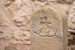 Halbrunder Grenzstein mit Kreuz und Hirschstange vor Natursteinmauer
