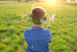 Fototapeta  - happy boy in wreath, floral crown on green sunlit meadow rear view, seen from behind, beauty nature and arrival summer, Midsummer celebration, tranquility nature, conveying sense awe, peace
