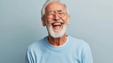 Fototapeta  - A man with a big smile on his face is wearing glasses and a blue shirt. He is laughing and he is happy. laughing old man, beard, glasses, happy, open laugh, enthusiastic, light blue sweater